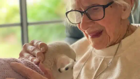Elderly woman smiling while holding a tiny rescue lamb named Vera